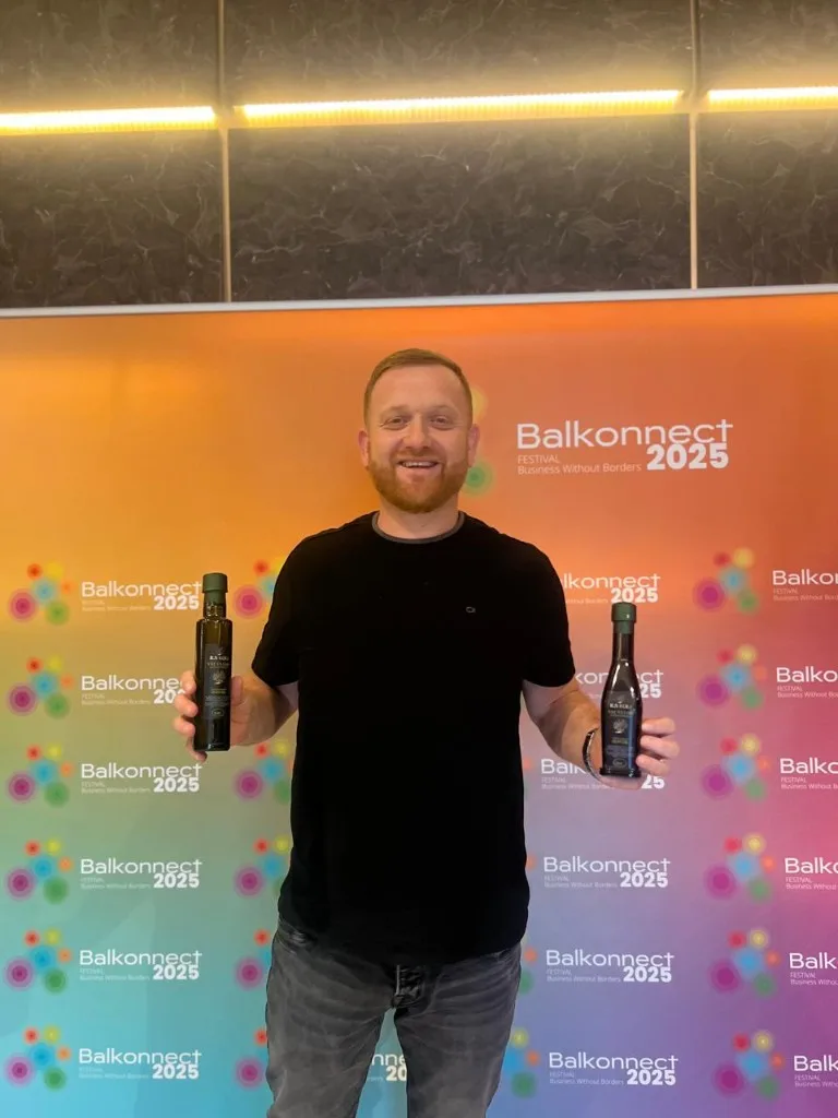 Smiling ambassador with two dark glass bottles of olive oil beside the Balkonnect step and repeat