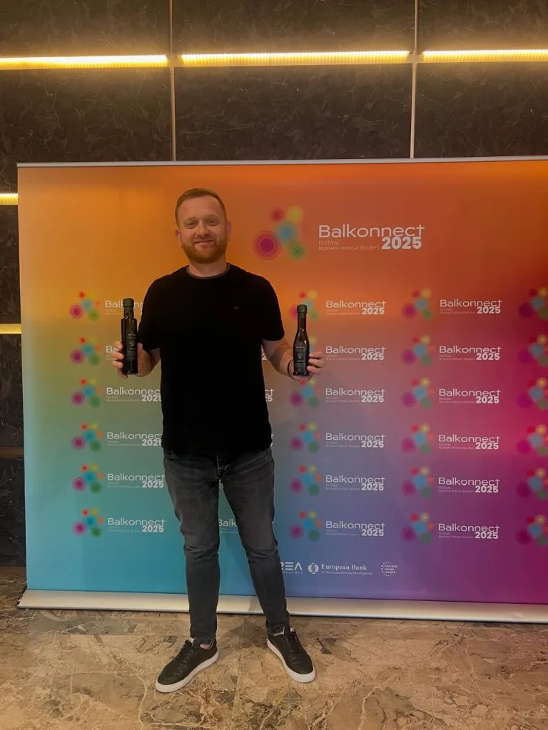 Presenter holding two bottles of R.S KOLI extra virgin in front of the Balkonnect Festival banner